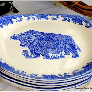 May include: A set of four white ceramic plates with a blue and white design of a cow. The plates have a scalloped edge and a blue and white floral border.