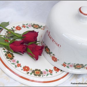Könnte beinhalten: Weiße Keramik-Käseglocke mit rotem und weißem Rand und dem Wort "cheese" auf der Seite. Die Glocke steht auf einem weißen Teller mit rotem und schwarzem Blumenmuster.