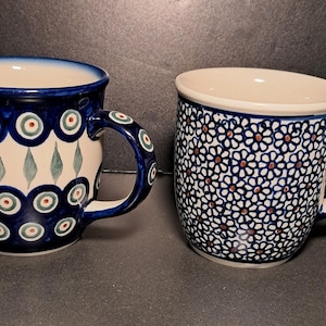 May include: Two ceramic mugs with blue and white patterns. One mug features a design of blue circles with green and red accents, while the other has a floral pattern. Both mugs have handles and are suitable for hot beverages.