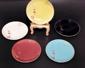 May include: Five small decorative plates with gold accents and floral designs. The plates are in various colors, including yellow, white, blue, and red.