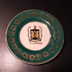 May include: A small, round, green and gold ceramic plate with a white center featuring a coat of arms with two lions and the text "In Fide Et In Bello Fortis" and "O'Carroll".