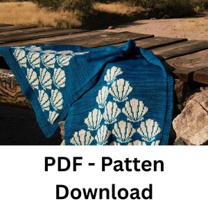 May include: A blue knitted blanket with a seashell pattern in white. The blanket is folded over a wooden surface. The text "PDF - Pattern Download" is at the bottom of the image.