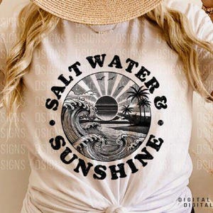 Pode incluir: Uma camiseta branca com um gr&aacute;fico circular preto que diz "Salt Water & Sunshine" com um sol, palmeiras e ondas dentro do c&iacute;rculo.