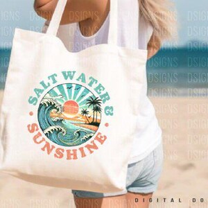 Pode incluir: Uma bolsa tote branca com um design gr&aacute;fico de um p&ocirc;r do sol sobre o oceano com ondas e palmeiras. O texto "Salt Water & Sunshine" est&aacute; escrito em um c&iacute;rculo ao redor do gr&aacute;fico.