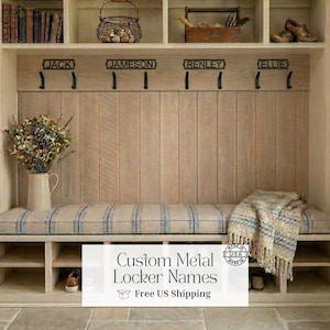 May include: A custom wooden entryway bench with a striped cushion, storage cubbies, and metal hooks labeled with names. The bench has a neutral color palette and is decorated with a vase of flowers and a blanket. The text on the image says "Custom Metal Locker Names".