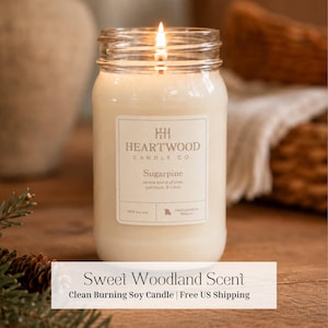 Puede incluir: Una vela de soja encendida en un frasco de vidrio transparente con una etiqueta blanca que dice Heartwood Candle Co. Sugarpine, serene blend of pine, patchouli, & citrus. La vela tiene una mecha encendida y cera de color blanco roto.