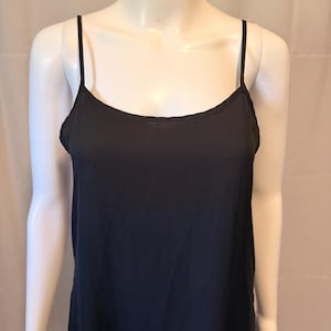 May include: A solid black camisole featuring a scoop neckline and thin spaghetti straps. The garment is displayed on a mannequin, showcasing a simple, sleeveless design with a straight hemline that falls below the waist, providing a clean look.