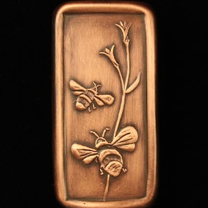 May include: A copper rectangular plaque with a raised design of two bees on a flower stem. The bees are detailed with wings, legs, and segmented bodies.