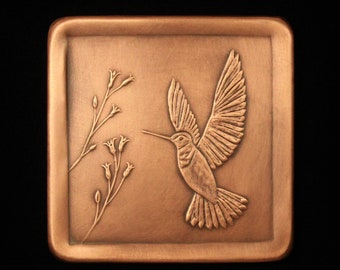 May include: A copper-colored metal plaque with a raised design of a hummingbird in flight, with a branch of flowers on the left side.