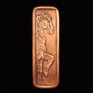 May include: A copper-colored rectangular plaque with a raised image of a horse's head and neck. The horse is facing to the left and has a long mane and a muscular neck.