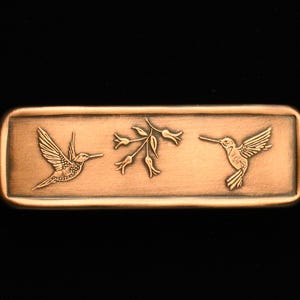 May include: A copper-colored rectangular bar with an etched design of two hummingbirds and a branch with buds.