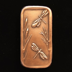 May include: A rectangular copper plaque with a raised design of two dragonflies and reeds. The dragonflies are in a bronze color.