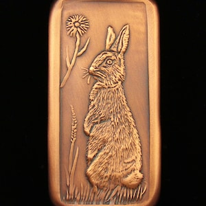 May include: A copper-colored rectangular plaque with a raised image of a rabbit standing on its hind legs. The rabbit is looking to the left and has a flower behind it.