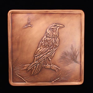 May include: A copper wall plaque with a detailed embossed image of a raven perched on a branch with pine needles. The raven is facing right and has a detailed feather pattern. The plaque has a brown patina and is signed "Weigel" in the lower right corner.