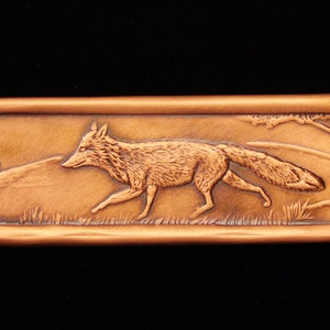 May include: A copper-colored rectangular plaque with an embossed image of a fox running through a grassy field. The fox is facing left and has a bushy tail. There is a small tree in the background.
