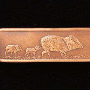 May include: A copper-colored rectangular plaque with a raised design of three peccaries walking in a line. The peccaries are in a natural brown color.