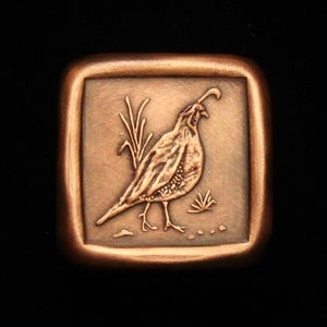 May include: A copper-colored square pendant with a raised image of a quail in a field of grass.