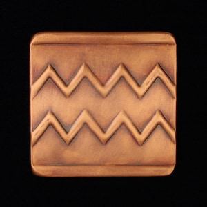 May include: A copper-colored square tile with a raised chevron pattern. The tile has a slightly textured surface.