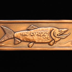 May include: A rectangular copper plaque with a detailed embossed image of a fish with its mouth open. The fish is swimming to the right and has scales and fins.