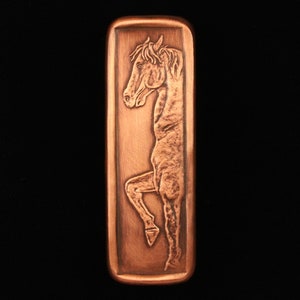 May include: A copper-colored rectangular plaque with a detailed relief sculpture of a horse's head and neck. The horse is facing left and has a mane and forelock. The plaque has a smooth, slightly textured surface.