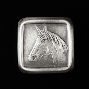 May include: A silver belt buckle with a detailed engraved image of a horse's head.