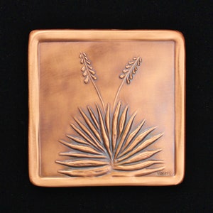 May include: A copper-colored square wall plaque with a raised design of a desert plant with two flower stalks. The plaque is signed "MOEPEL" in the lower right corner.