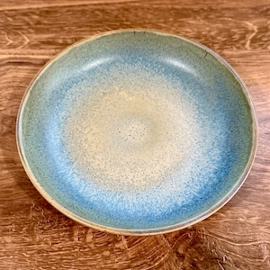 May include: A round ceramic bowl with a gradient of colors. The bowl transitions from a light yellow center to a blue and green rim. The bowl is likely used for serving food.