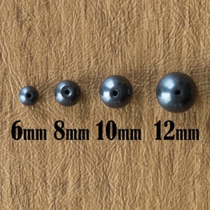 May include: Four black round beads of different sizes, 6mm, 8mm, 10mm, and 12mm, arranged in a row on a brown surface.