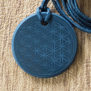May include: A black pendant with a carved flower of life design, hanging on a black cord.