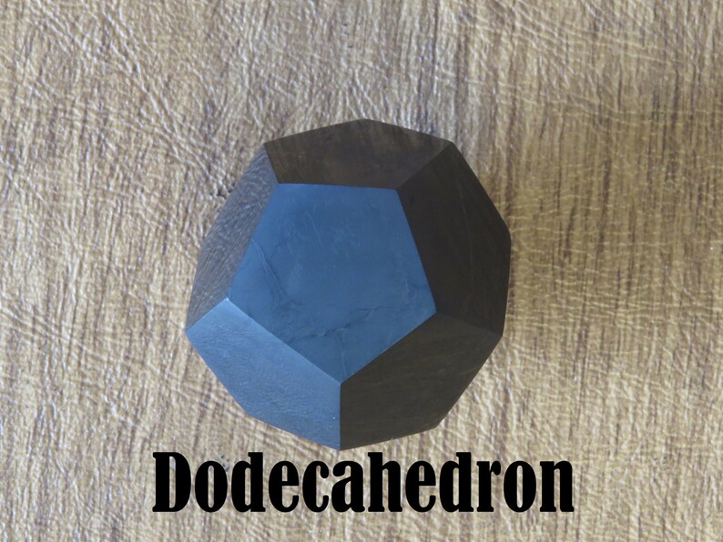 May include: A dark blue wooden dodecahedron, a twelve-sided geometric shape, on a light brown textured surface. The word "Dodecahedron" is written in black below the shape.
