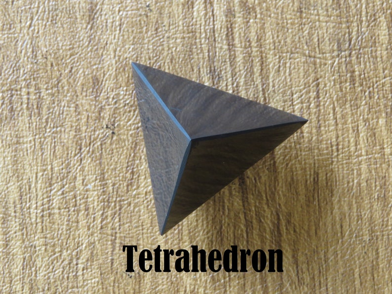 May include: A dark brown wooden tetrahedron, a geometric shape with four triangular faces. The tetrahedron is resting on a light brown surface.