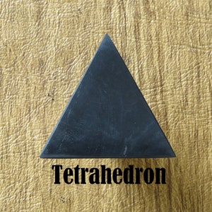 May include: A black tetrahedron, a geometric shape with four triangular faces, is shown on a textured, light brown surface. The word "Tetrahedron" is written in black below the shape.