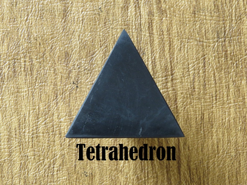 May include: A black tetrahedron, a geometric shape with four triangular faces, is shown on a textured, light brown surface. The word "Tetrahedron" is written in black below the shape.