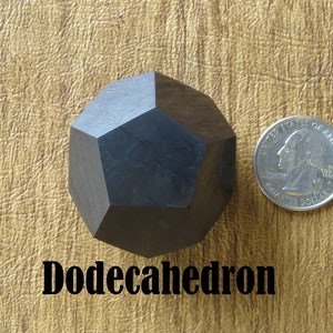 May include: A black wooden dodecahedron, a twelve-sided geometric shape, is shown next to a US quarter for size comparison. The text "Dodecahedron" is printed below the object.