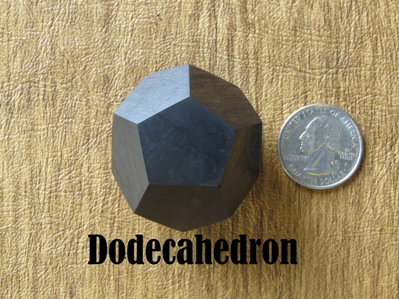 May include: A black wooden dodecahedron, a twelve-sided geometric shape, is shown next to a US quarter for size comparison. The text "Dodecahedron" is printed below the object.