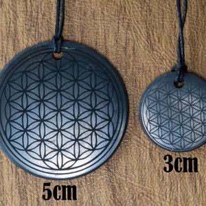 May include: Two black stone pendants with a flower of life design. The larger pendant is 5 cm in diameter and the smaller pendant is 3 cm in diameter.