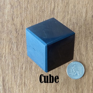 May include: A black cube with a smooth, polished surface. The cube is about the size of a US quarter.