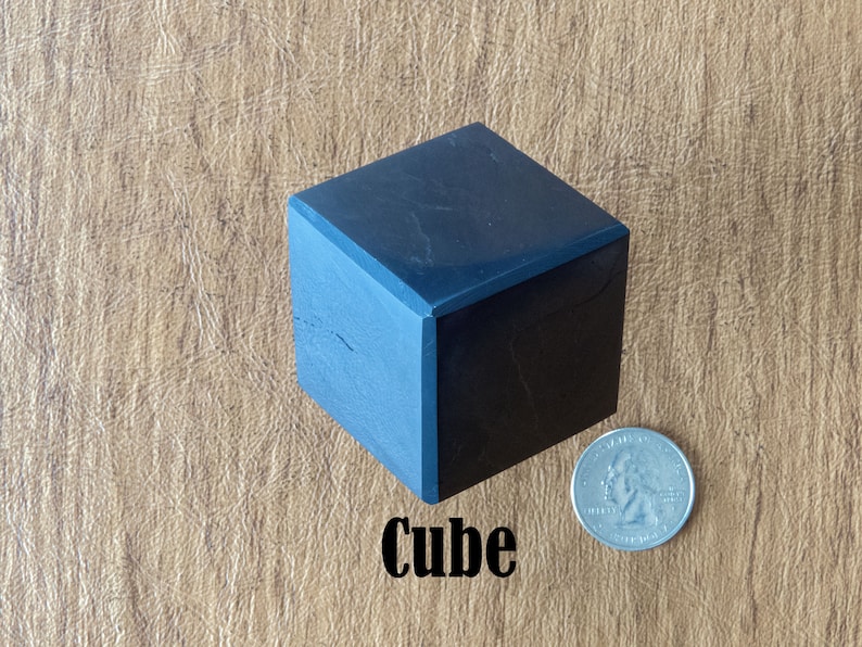 May include: A black cube with a smooth, polished surface. The cube is about the size of a US quarter.