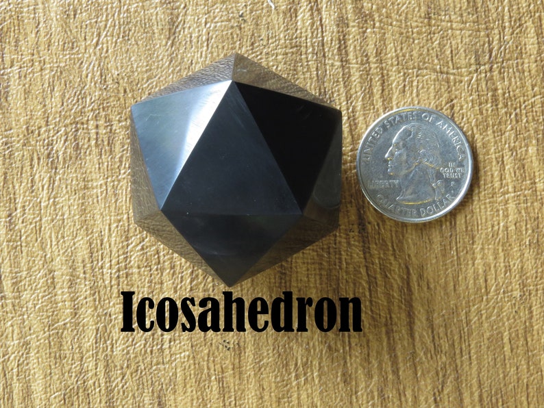 May include: A black icosahedron, a 20-sided geometric shape, is shown next to a US quarter for size comparison. The icosahedron is made of a smooth, polished material.