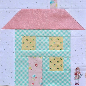 May include: A pink and blue patchwork quilt block featuring a house with a gingham roof and windows. The house is surrounded by a white background with green polka dots.