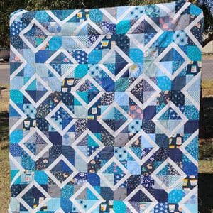 Pode incluir: Um edredom azul e branco com um padrão geométrico. O edredom é feito de quadrados e triângulos, e tem um fundo branco com detalhes azuis. O edredom é feito de tecido com diferentes padrões, incluindo florais, geométricos e abstratos.