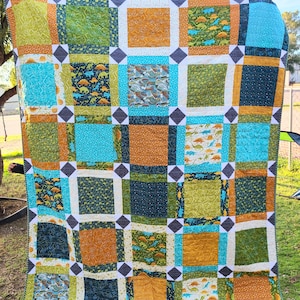May include: A patchwork quilt featuring a dinosaur theme. The quilt is made up of squares of different fabrics, each with a different dinosaur pattern. The quilt is in shades of blue, green, orange, and white.