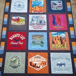 以下が含まれることがあります： 国立公園の画像が描かれた正方形の手作りキルト。バッドランズ、グランドキャニオン、ラシュモア山、イエローストーンのデザインが含まれています。キルトは青、オレンジ、グレーの生地で縁取られています。