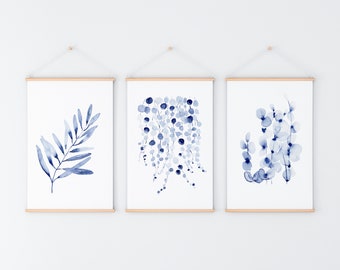 Può includere: Tre stampe ad acquerello con illustrazioni botaniche blu. Le stampe sono incorniciate con una cornice in legno naturale e appese a una parete bianca.