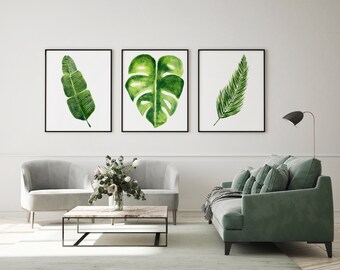 Könnte beinhalten: Drei gerahmte Aquarellbilder von tropischen Blättern. Die Bilder hängen an einer weißen Wand über einem grauen Sofa und einem grünen Sofa. Das Sofa steht in einem Wohnzimmer mit einem Couchtisch davor.