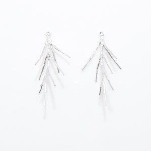 以下が含まれることがあります： 繊細な枝のようなデザインのシルバー製のイヤリングのペア。各イヤリングは、小さなループから伸びる複数の細いテクスチャ加工された枝を特徴としています。
