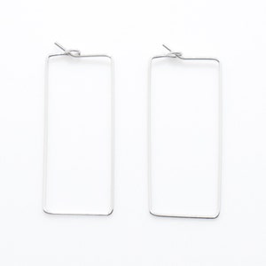 May include: A pair of silver rectangular hoop earrings.