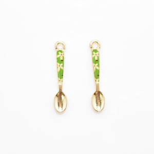 Puede incluir: Dos cucharas doradas en miniatura con diseños florales verdes y blancos en los mangos.