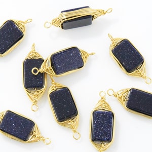 May include: Gold-colored wire-wrapped pendants with rectangular, dark blue, glittery stones. The pendants are arranged on a white surface, showcasing their intricate wirework and the sparkling stones.