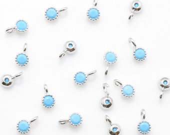 May include: A collection of 17 silver-toned charms with light blue round stones. Each charm has a loop for attaching to a necklace or bracelet.